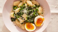 a white bowl filled with pasta, eggs and spinach on top of a table