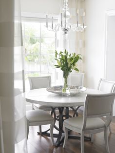 a dining room table with chairs and a vase on it's centerpiece in front of a window