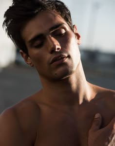 a shirtless man holding his chest in front of the camera and looking off into the distance