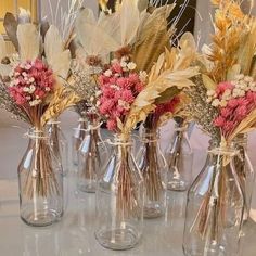 four clear vases with dried flowers in them on a table top next to a mirror