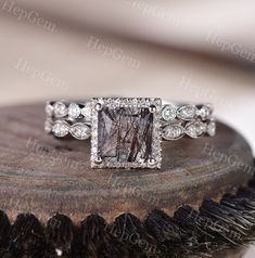 an engagement ring with a square cut diamond surrounded by small round diamonds on top of a piece of wood