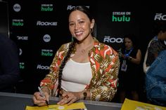 a woman sitting at a table signing autographs for people to watch on rokuo