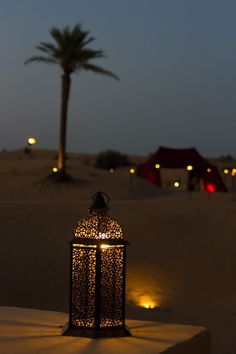 a lantern lit up in the desert at night with palm trees and tents in the background