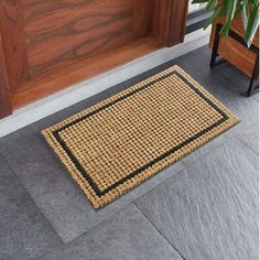 a close up of a door mat on the ground near a potted plant in front of a wooden door