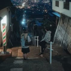 two people are sitting on the stairs at night with city lights in the back ground