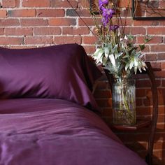 a vase filled with flowers sitting on top of a bed next to a brick wall