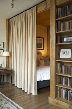 a bed sitting next to a tall book shelf filled with books on top of a hard wood floor