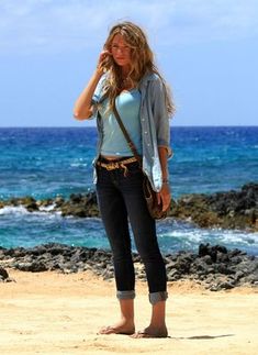 a woman standing on top of a sandy beach next to the ocean talking on a cell phone