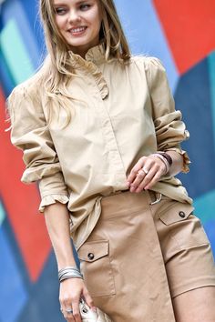 Some shirts simply make you happy the moment you slip them on. This whimsical blouse is one of them. With its ruffle-trimmed collar and sleeves adding a playful touch, this button-down beauty conjures images of twirling through a field of wildflowers on a perfect summer day. Yet its crisp cotton fabric and tailored cut mean it works just as well for that important meeting or client lunch. Versatile, flattering and mood-boosting all at once, this blouse pulls double duty as both a style staple an Trendy Spring Blouse With Ruffled Collar, Cotton Button-up Blouse With Smocked Cuffs, Spring Button-up Blouse With Smocked Cuffs, Spring Daywear Beige Shirt, Spring Beige Shirt For Daywear, Trendy Ruffled Collar Top, Chic Shirt With Ruffled Collar And Details, Chic Shirt With Ruffled Collar And Ruffles, Workwear Top With Ruffled Collar And Buttons