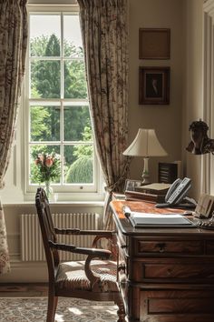 a desk and chair in front of a window with drapes on the windowsill