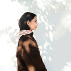 a woman standing in front of a tree with her back to the camera and wearing a scarf around her neck