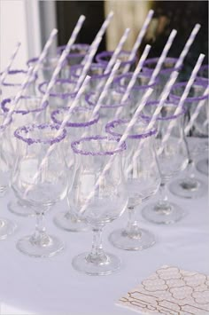 many wine glasses are lined up on a table with paper straws in them and purple confetti sticks sticking out of the top