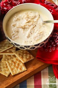 a bowl of soup and crackers on a wooden cutting board with a red napkin