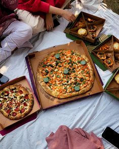 several pizzas and appetizers are sitting on a table with people around them