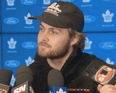 a man wearing a black hat and holding microphones in front of a blue wall