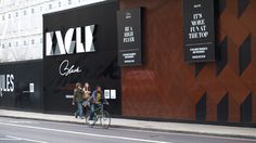 two people riding bikes down the street in front of a building with black and white lettering on it