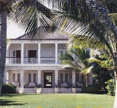 a large white house with palm trees in the front yard and two balconies