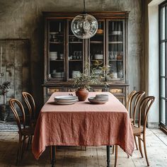 a dining room table with plates and bowls on it, in front of an old china cabinet