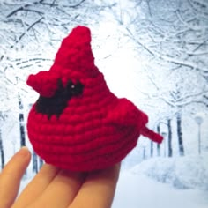 a crocheted red bird sitting on top of a persons hand in the snow