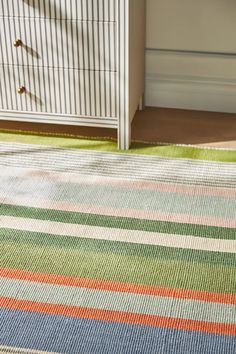 a multicolored rug on the floor next to a white dresser and chest of drawers