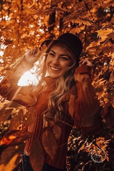 a woman wearing a hat standing in front of some trees with leaves on it and the sun shining behind her