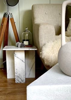 a living room with a chair, lamp and marble side table in front of it