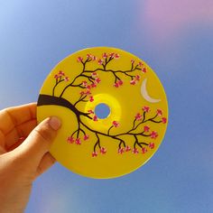 a hand holding a yellow plate with pink flowers on it and a moon in the sky