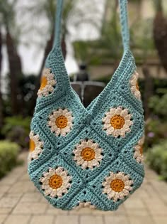 a crocheted bag hanging from a hook on a brick walkway in front of some trees