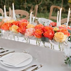 an arrangement of flowers and candles on a long table with place settings for the dinner guests