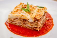 a piece of lasagna on a white plate with sauce and green garnish