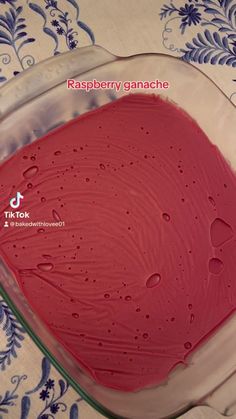 a pink cake in a glass dish on a blue and white tablecloth with the words raspberry ganache