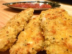 two pieces of fried chicken sitting on top of a wooden table next to a bowl of ketchup