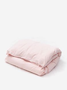 a pink comforter is folded on top of a white bed sheet and pillowcase