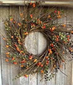 a wreath made out of twigs and orange flowers on a wooden door with red berries