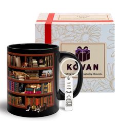 a black coffee mug sitting next to a book shelf with books on it and a gift box