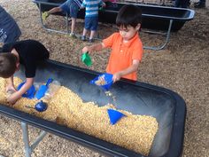 two young boys are playing in a sandbox filled with corn at an outdoor event