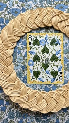 a close up of a woven frame on a wall with blue and green flowers in the background