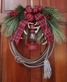 a christmas wreath hanging on the front door with a cow horn and pine needles attached to it