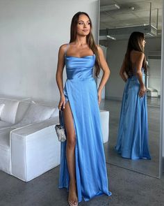 a woman standing in front of a mirror wearing a blue dress with thigh high slit