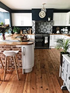 a kitchen with wooden floors and white cabinets is pictured in this image, there are two stools at the center of the island