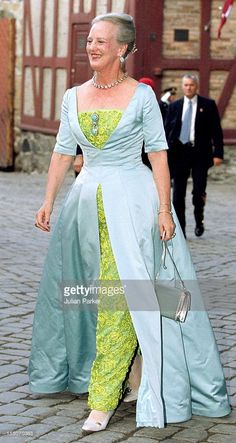 an older woman in a blue and green dress walking down the street with her purse