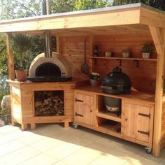 an outdoor kitchen made out of wood with grill and oven on the outside wall, surrounded by greenery