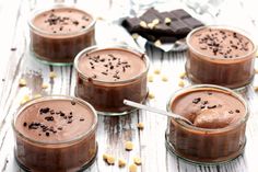 four glasses filled with chocolate pudding sitting on top of a wooden table next to candy bars