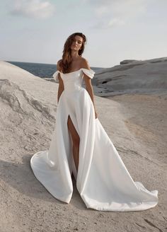 a woman standing on top of a sandy beach wearing a white dress with thigh high slit