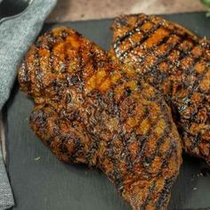 two pieces of grilled meat sitting on top of a cutting board next to a knife