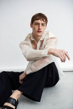 a man sitting on the ground with his arms crossed and legs crossed, wearing black sandals