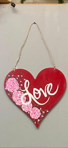 a red heart hanging on the side of a wall with pink roses painted on it