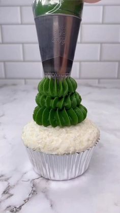 a cupcake with frosting and green leaves on top is being held up by a hand