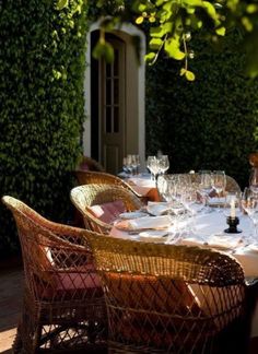 an outdoor dining area with wicker chairs and table set for four, surrounded by greenery