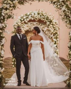 a bride and groom standing under an arch with flowers on it at the end of their wedding day